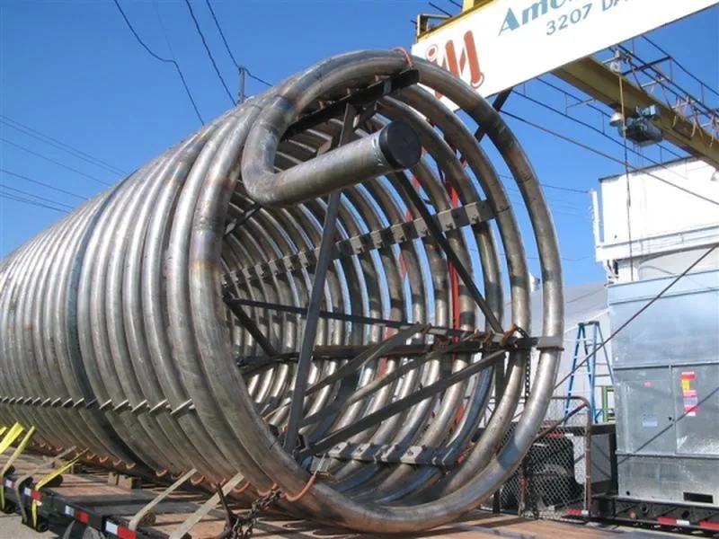 A large helical pipe coil loaded on a trailer beside the company crane in the Dawson Road yard