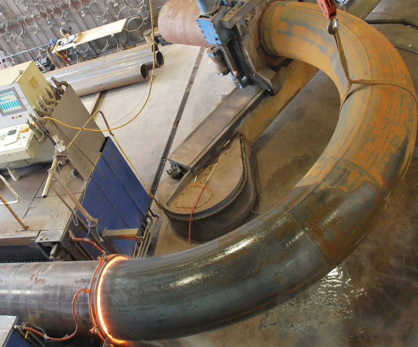 A large-diameter pipe in the induction bending machine, the heat band glowing as the bend is formed
